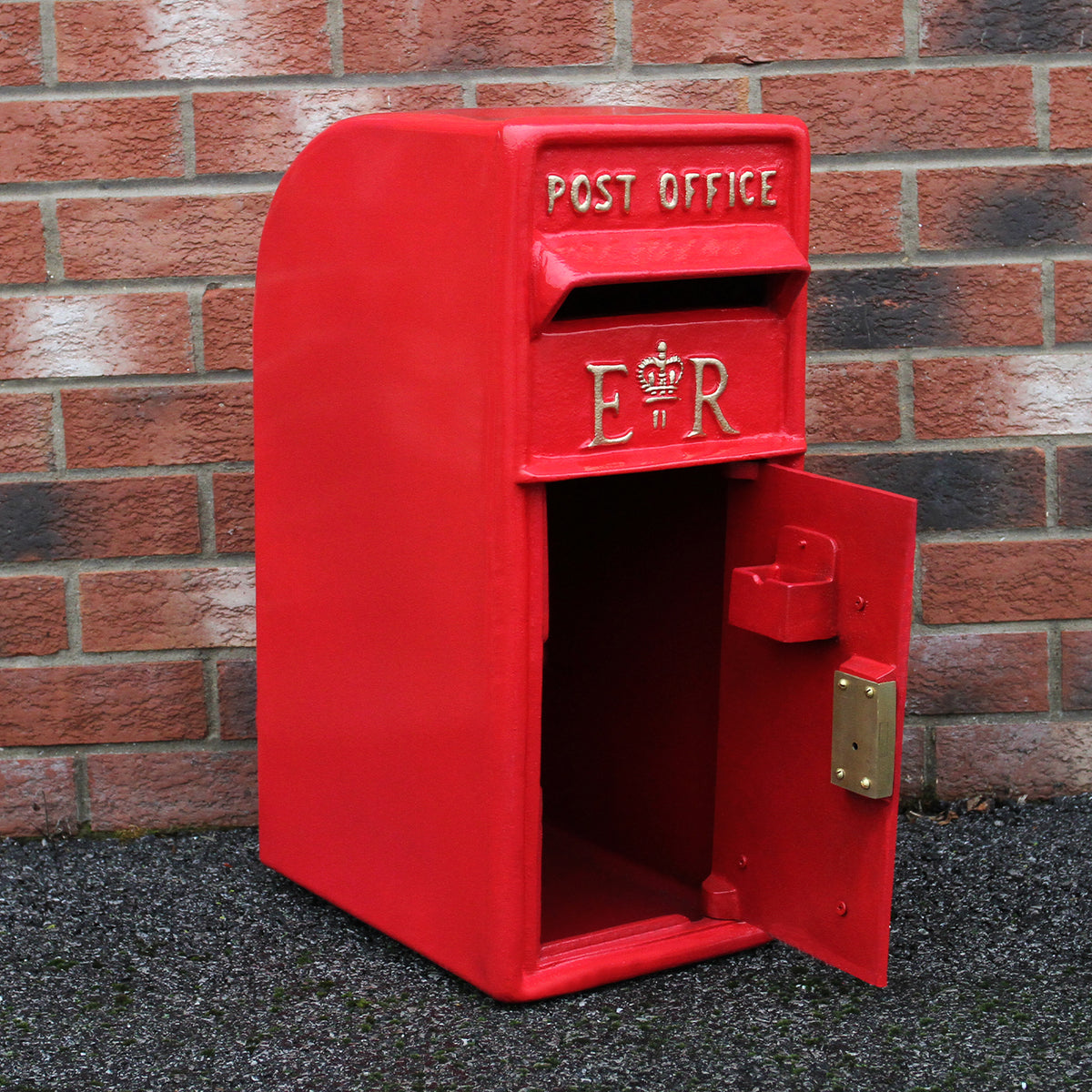 Roter Briefkasten im englischen Stil mit goldener „ER“-Prägung, glänzender Oberfläche und offenem Fach vor einer Backsteinmauer