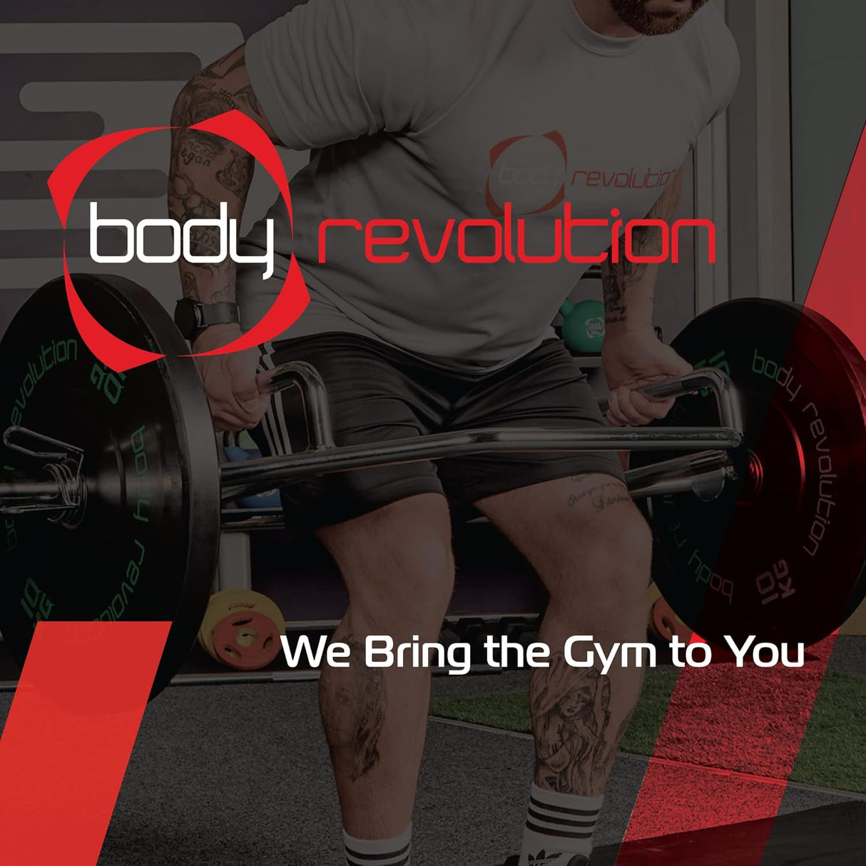 Ein Mann hebt eine schwere Hantel im Fitnessstudio, trägt ein graues T-Shirt mit dem Logo von Body Revolution und hat tätowierte Arme