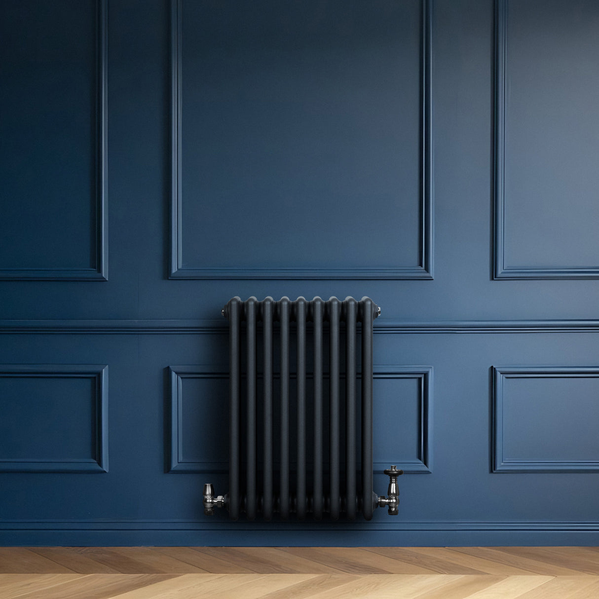 Röhrenheizkörper mit vier Säulen in Anthrazitgrau, elegant an einer blauen Wand montiert, ergänzt durch Holzfußboden und stilvolle Armaturen