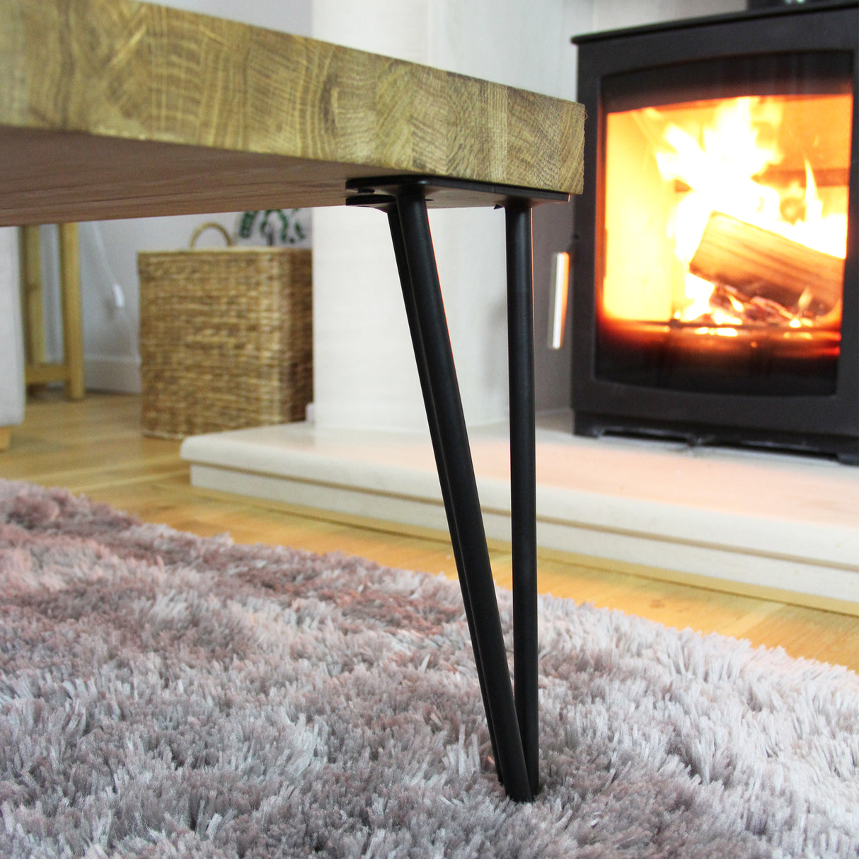 Schwarze Hairpin Tischbeine aus Rohstahl mit zwei Streben, elegant unter einem Holztisch, vor einem gemütlichen Kaminfeuer auf einem flauschigen Teppich