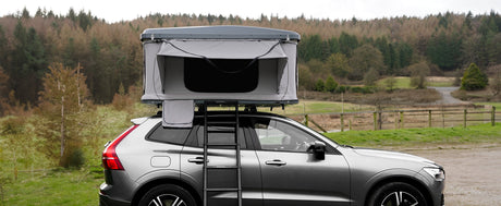 Ein graues Autodachzelt auf einem SUV, umgeben von einer grünen Waldlandschaft, bietet eine praktische und stilvolle Campinglösung für Abenteuerlustige