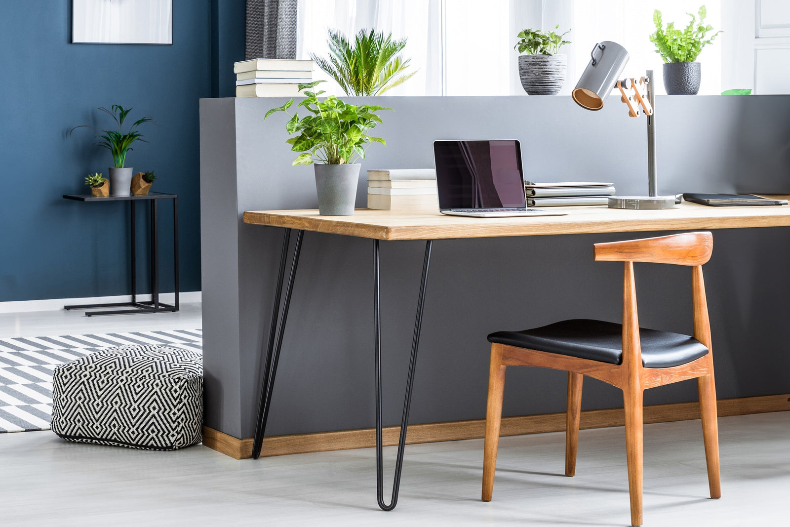 Ein stilvoller Schreibtisch aus hellem Holz mit schwarzen Hairpin-Tischbeinen, einem Laptop, einer Lampe und Pflanzen in modernen Töpfen