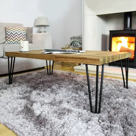Holztisch mit Hairpin-Beinen, rustikaler Eichenoberfläche, auf einem weichen, grauen Teppich, vor einem modernen Kamin