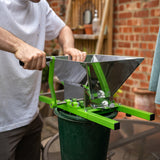 Tragbarer Obstzerkleinerer mit Kurbel in glänzendem Edelstahl und grünem Gestell, ideal zum Zerkleinern von Obst in einem Eimer