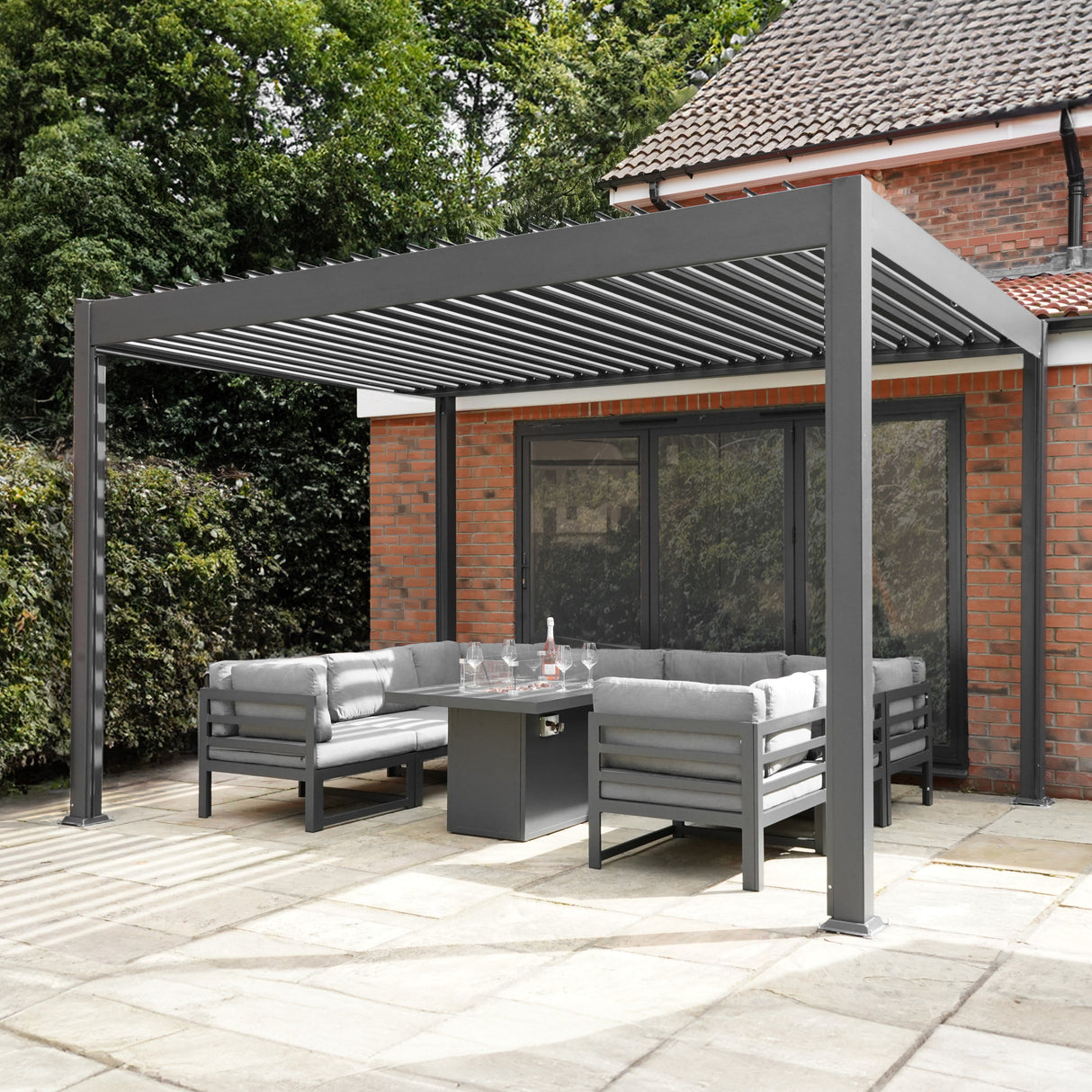 Anthrazitfarbene Aluminium-Pergola mit LED-Beleuchtung, 3 m x 3 m, umgeben von modernen grauen Sofas und einem eleganten Tisch auf einem gepflasterten Boden