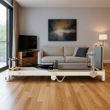 Pilates Reformer Maschine aus Aluminium in einem modernen Wohnzimmer mit Holzfußboden, grauem Sofa und Fernseher im Hintergrund