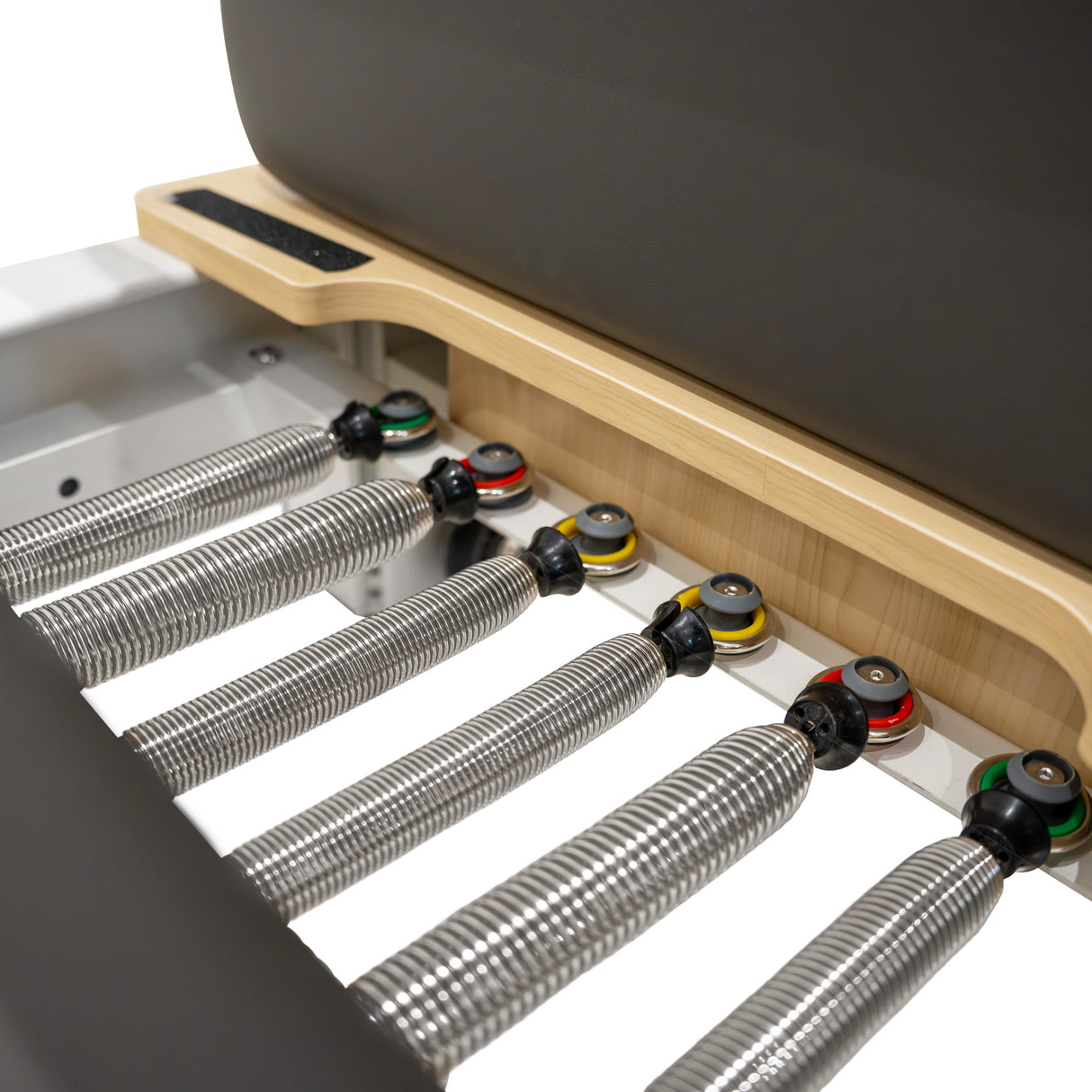 Pilates Reformer Maschine aus Aluminium mit Holzdetails, elastischen Federn in verschiedenen Farben und einem gepolsterten, grauen Sitz für Komfort und Stabilität