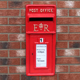 Roter Briefkasten im englischen Stil mit goldenen Details, auf Ziegelmauer montiert, zeigt Abholzeiten und königliches Emblem