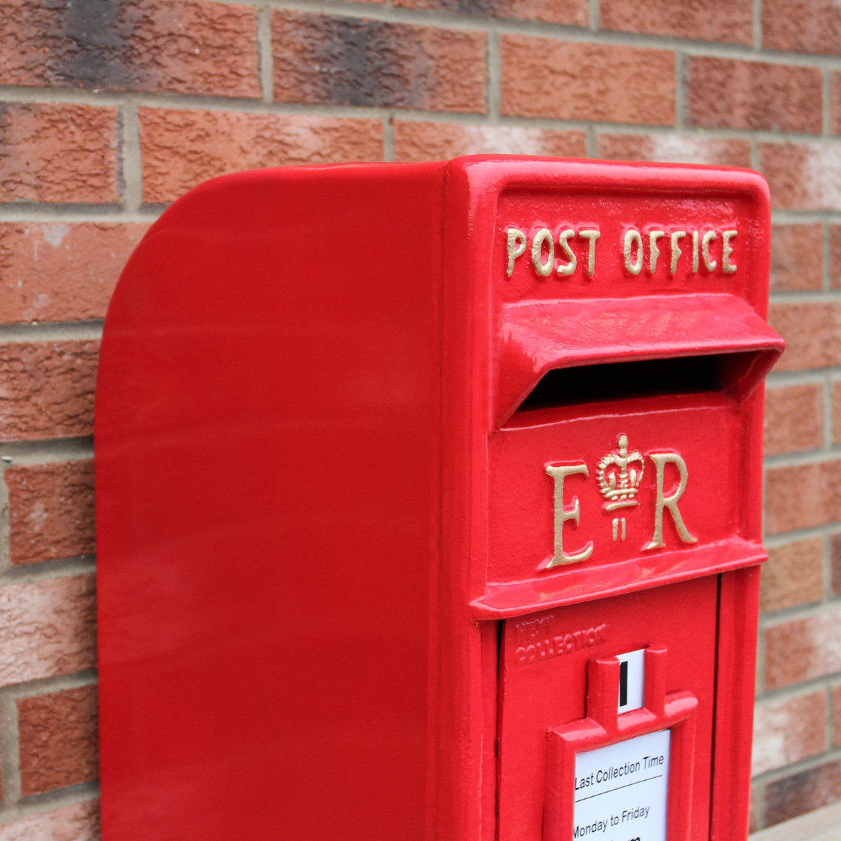 Roter Briefkasten mit Bodenständer, glänzende Oberfläche, goldene Schriftzüge "POST OFFICE" und "ER", vor einer Ziegelmauer