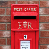 Roter Briefkasten im englischen Stil mit goldenen Buchstaben und Krone, vor einer Backsteinmauer, samtenes Finish und klassisches Design