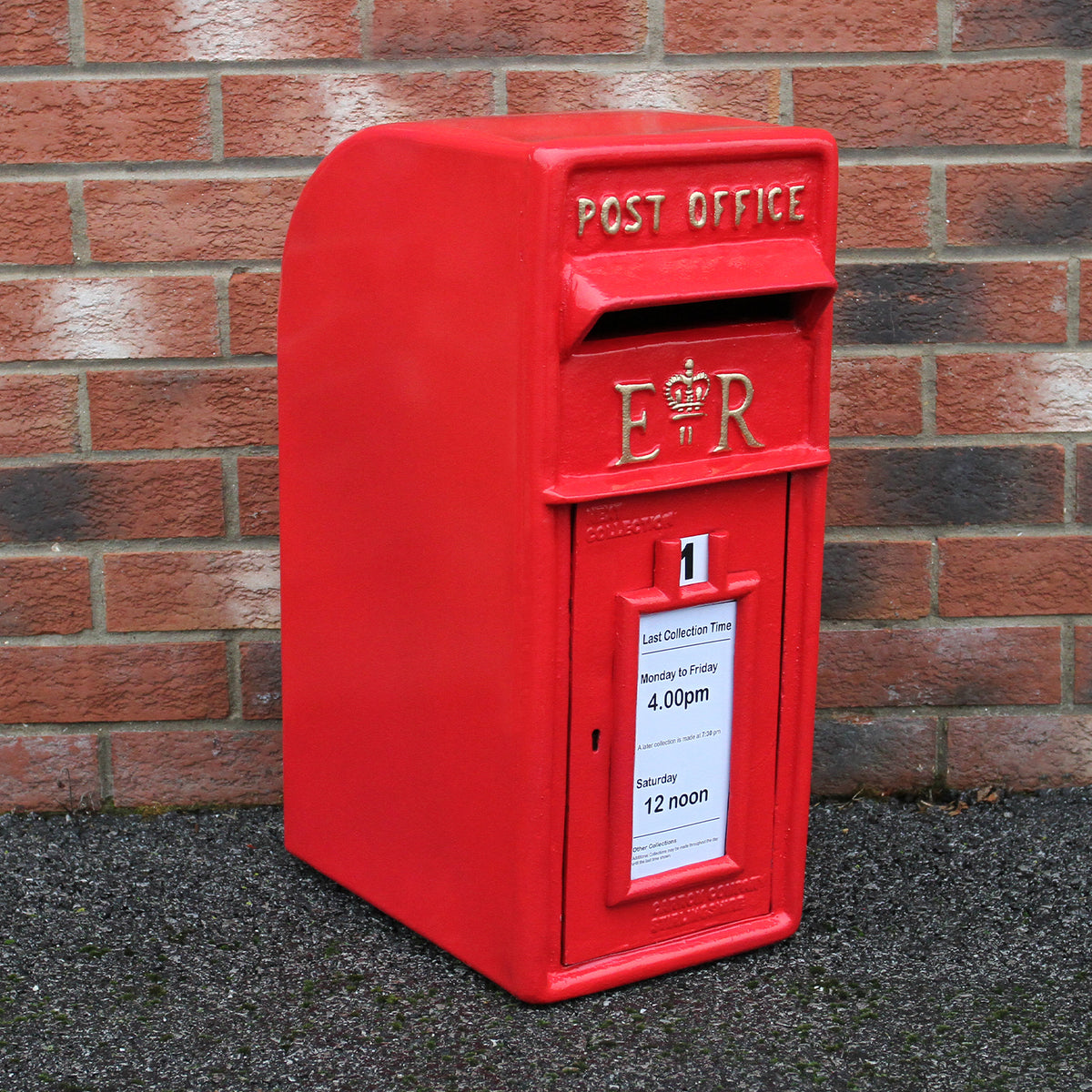 Roter Briefkasten im englischen Stil mit glänzender Oberfläche, königlichem Wappen und Sammelzeiten auf einem weißen Schild