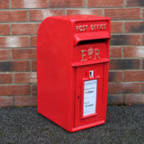 Roter Briefkasten im englischen Stil mit glänzender Oberfläche, königlichem Wappen und Sammelzeiten auf einem weißen Schild