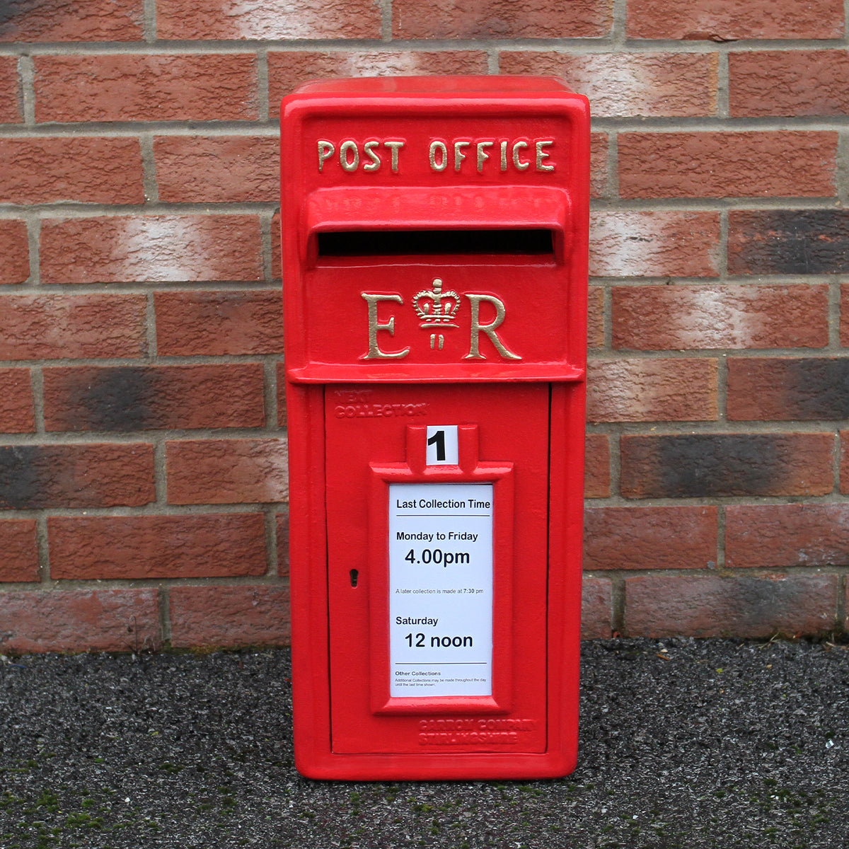 Roter Briefkasten im englischen Stil mit goldenen Buchstaben, verziert mit einer Krone, vor einer Backsteinmauer platziert