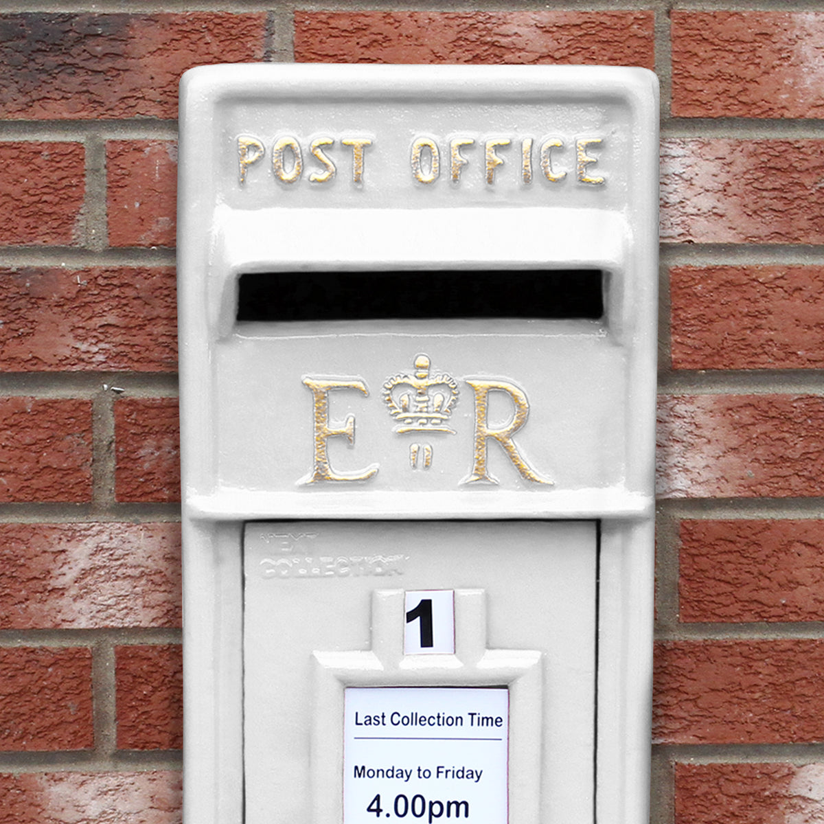 Weißer Briefkasten mit Bodenständer, goldene Buchstaben "POST OFFICE" und "E R", auf rotem Ziegelmauerwerk platziert