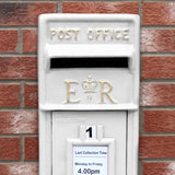 Weißer Briefkasten mit Bodenständer, goldene Buchstaben "POST OFFICE" und "E R", auf rotem Ziegelmauerwerk platziert