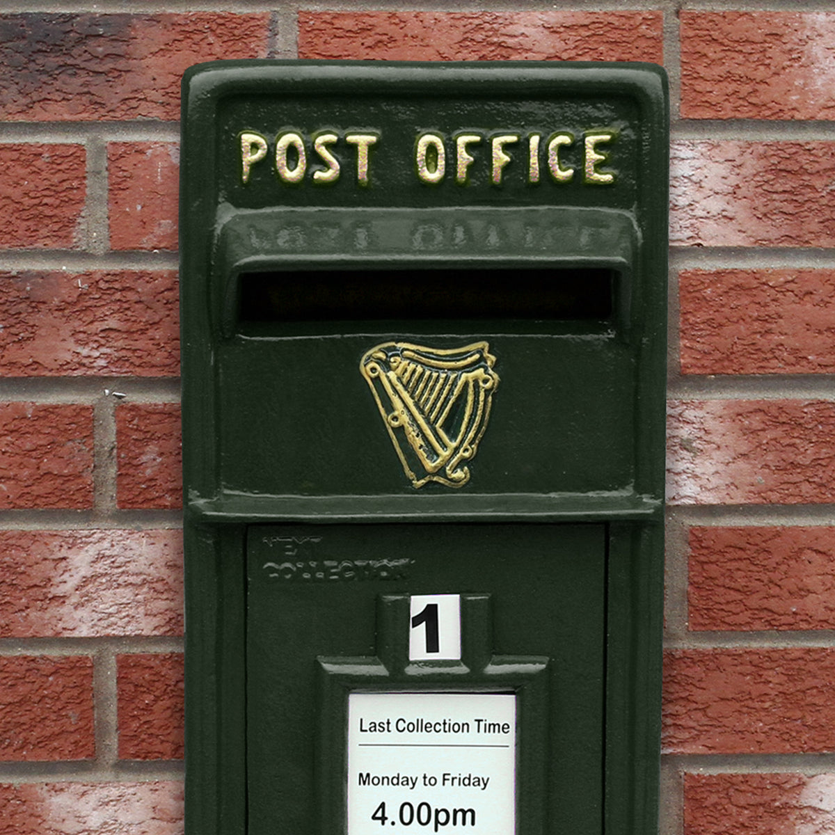 Grüner Briefkasten mit Bodenständer, goldene Schrift "POST OFFICE", Harfenmotiv, auf Backsteinmauer platziert