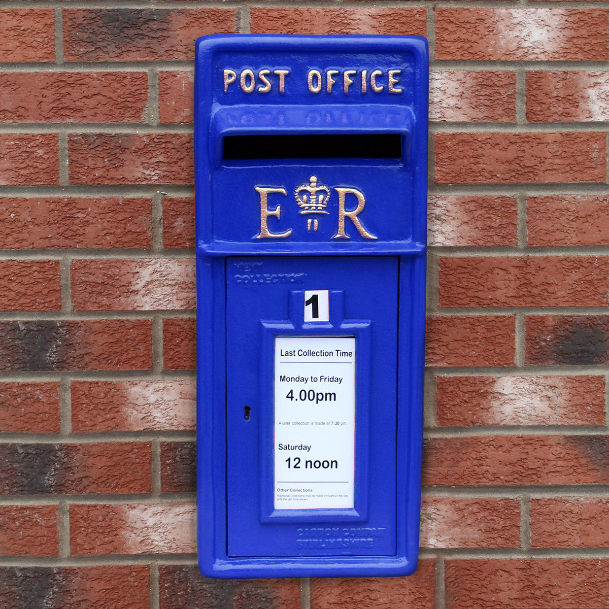 Blauer Briefkasten mit Bodenständer, verzierte Oberfläche, goldene Schrift und Krone, an einer roten Ziegelwand montiert