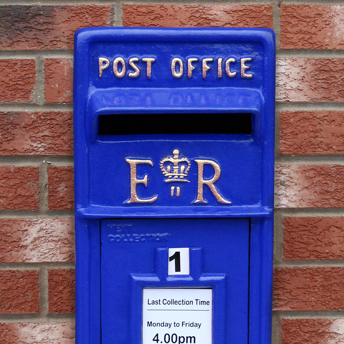 Blauer Briefkasten mit Bodenständer, robuste Struktur, goldene Schriftzüge und Krone, vor einer roten Ziegelwand platziert
