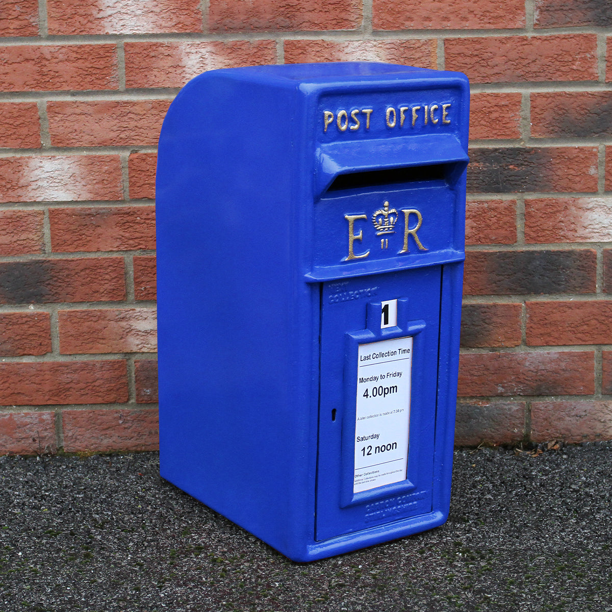 Blauer Briefkasten mit Bodenständer, klassisches Design, glänzende Oberfläche, auf grauem Untergrund vor Backsteinmauer platziert