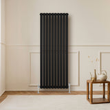 Schwarzer Gliederheizkörper mit TRV Chromventilen, 1600mm x 600mm, elegant an einer hellen Wand, ergänzt durch einen modernen Holztisch und Dekoration