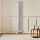 Hochformatiger, weißer Gliederheizkörper mit TRV Chromventilen, elegant an einer hellen Wand montiert, vor einem stilvollen Holztisch und Teppich