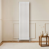 Hochformatiger, weißer Gliederheizkörper mit TRV Chromventilen, elegant an einer hellen Wand montiert, ergänzt durch einen stilvollen Holztisch im Vordergrund