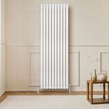 Hochformatiger, weißer Gliederheizkörper mit TRV Chromventilen, elegant an einer hellen Wand montiert, neben einem Holzkaffee-Tisch in modernem Raum