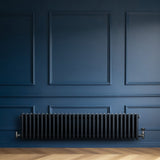 Röhrenheizkörper mit vier Säulen in Anthrazitgrau, elegant und modern, montiert an einer blauen Wand, ergänzt durch einen hellen Holzfußboden