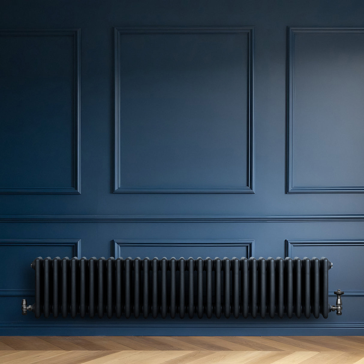 Röhrenheizkörper mit vier Säulen in anthrazitgrau, elegant und modern, an einer blauen Wand montiert, ergänzt durch einen hellen Holzfußboden