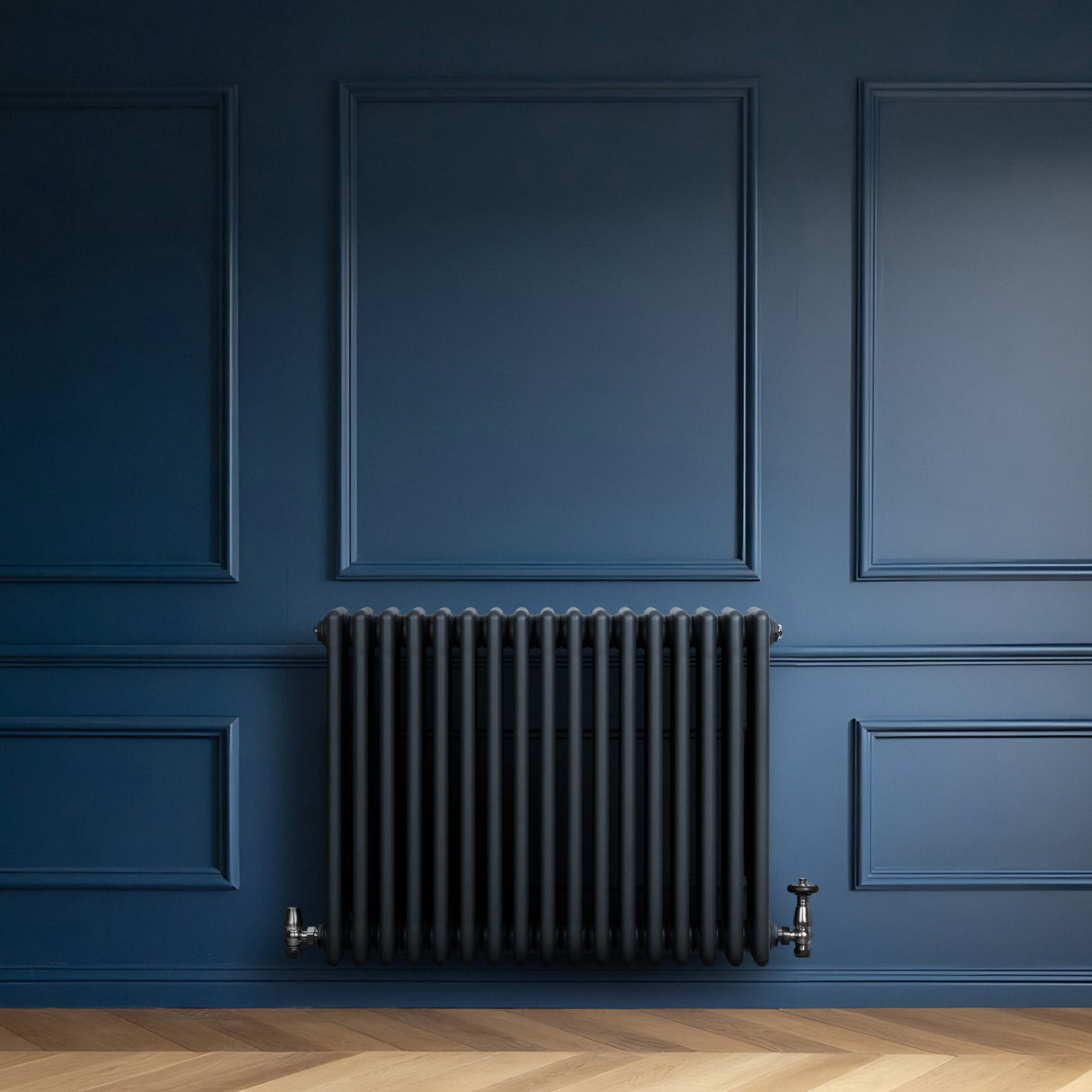 Röhrenheizkörper mit vier Säulen in Anthrazitgrau, elegant an einer blauen Wand montiert, ergänzt durch einen modernen, minimalistischen Stil