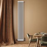 Hochformatiger, eleganter Röhrenheizkörper mit vier Säulen in strahlendem Weiß, montiert an einer warmen, beige Wand, neben einem stilvollen Esstisch