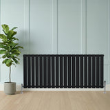 Flachheizkörper in Schwarz, 600mm x 1400mm, mit vertikalen Lamellen und eleganten Füßen, vor einer hellen Wand und einer Pflanze in einem Topf