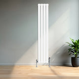 Flachheizkörper in Weiß, 1600mm x 280mm, mit glatten, vertikalen Lamellen und glänzenden, verchromten Ventilen, vor einer hellen Wand und Pflanzen im Hintergrund