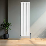 Flachheizkörper in Weiß, 1600mm x 420mm, mit vertikalen Lamellen und glänzenden, verchromten Ventilen, vor einer modernen Wand und Pflanzen im Hintergrund