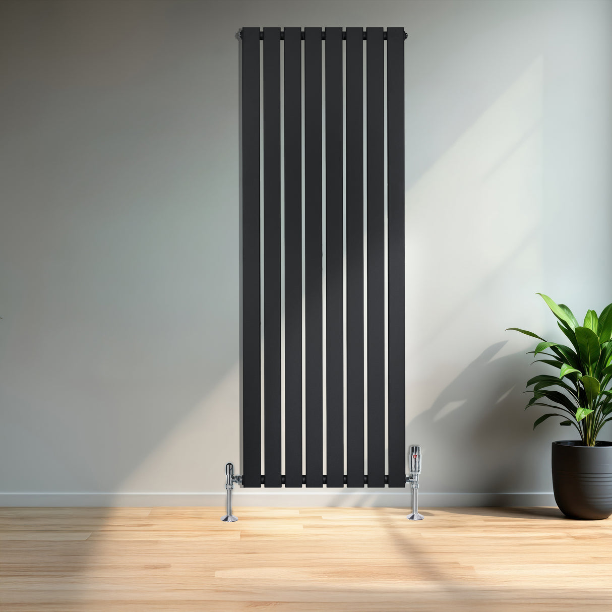 Schmaler, vertikaler Flachheizkörper in elegantem Schwarz, 1600mm x 560mm, mit glänzenden Füßen, vor einer hellen Wand und einer Pflanze im Topf
