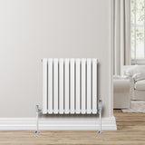 Weißer Gliederheizkörper mit 600mm x 600mm, vertikalen Lamellen und glänzenden Ventilen, vor einer hellen Wand und einem gemütlichen Raum
