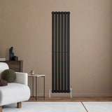 Schwarzer Gliederheizkörper mit sechs vertikalen Röhren, elegant an einer beige Wand montiert, ergänzt durch moderne Möbel und Dekoration