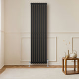 Schwarzer Gliederheizkörper mit sechs vertikalen Röhren, 1800mm x 480mm, elegant an einer hellen Wand montiert, ergänzt durch einen modernen Holztisch