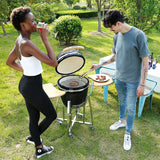 Kamado Holzkohlegrill 18" in Schwarz, mit geöffnetem Deckel, während zwei Personen im Freien grillen und Getränke genießen, umgeben von grünem Gras