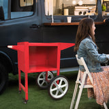 Roter KuKoo Popcornmaschinenwagen mit großen silbernen Rädern, auf einer grünen Wiese neben einem Foodtruck, ideal für Veranstaltungen und Partys
